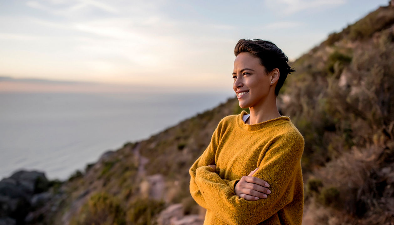woman in yellow sweater standing alongside a coast/cliff